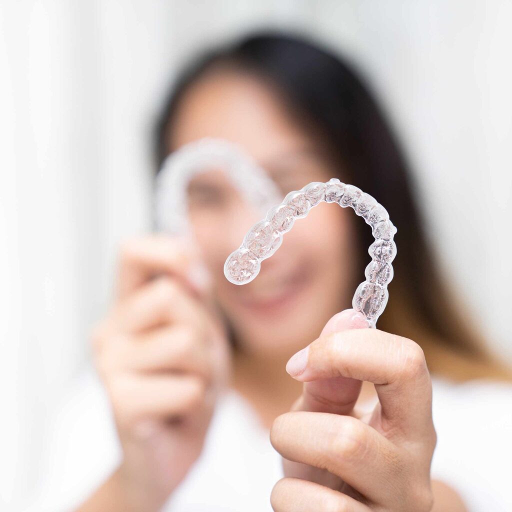 photo of a gal holding orthodontic clear aligners like Invisalign or Clarity Aligners.